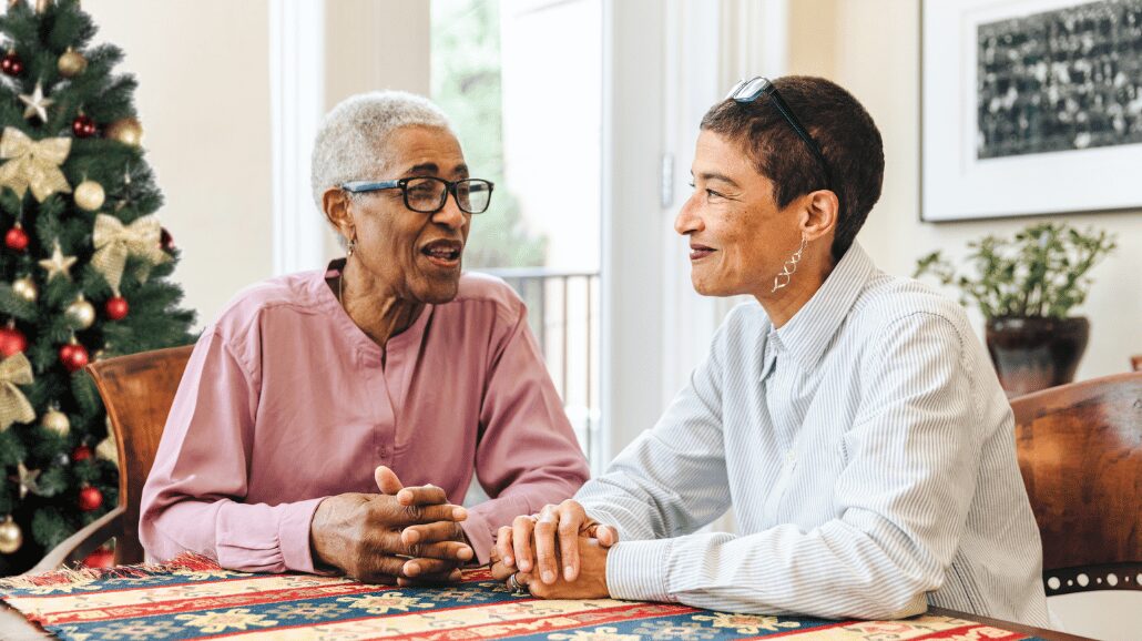 Senior mother with adult daughter talking at kitchen table