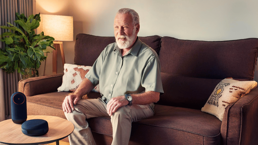 Senior man sitting on a couch with a voice-activated device onthe coffee table