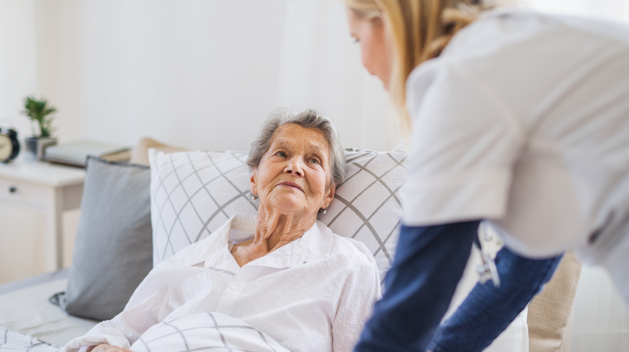 Sick elderly in bed with a caregiver next to her