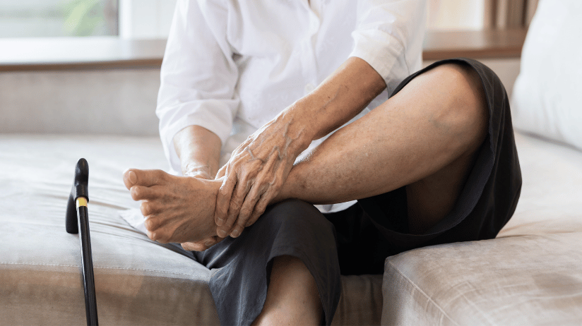 Elderly person sitting on a bed rubbing their feet