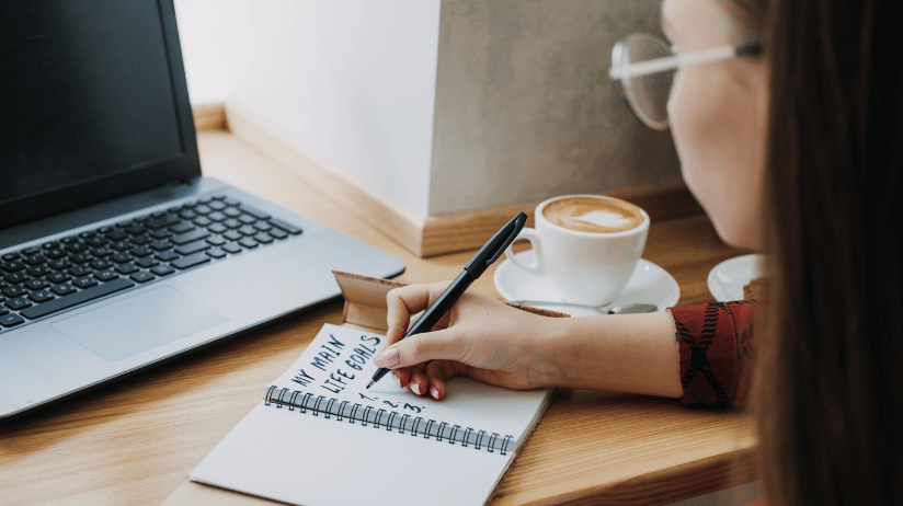 Young female looking at a computer and writing down life goals