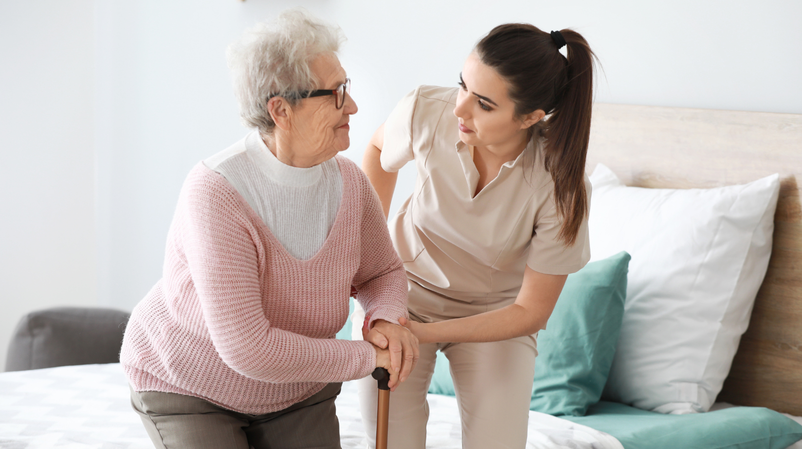 Caregiver helping a senior woman get out of bed with a cane