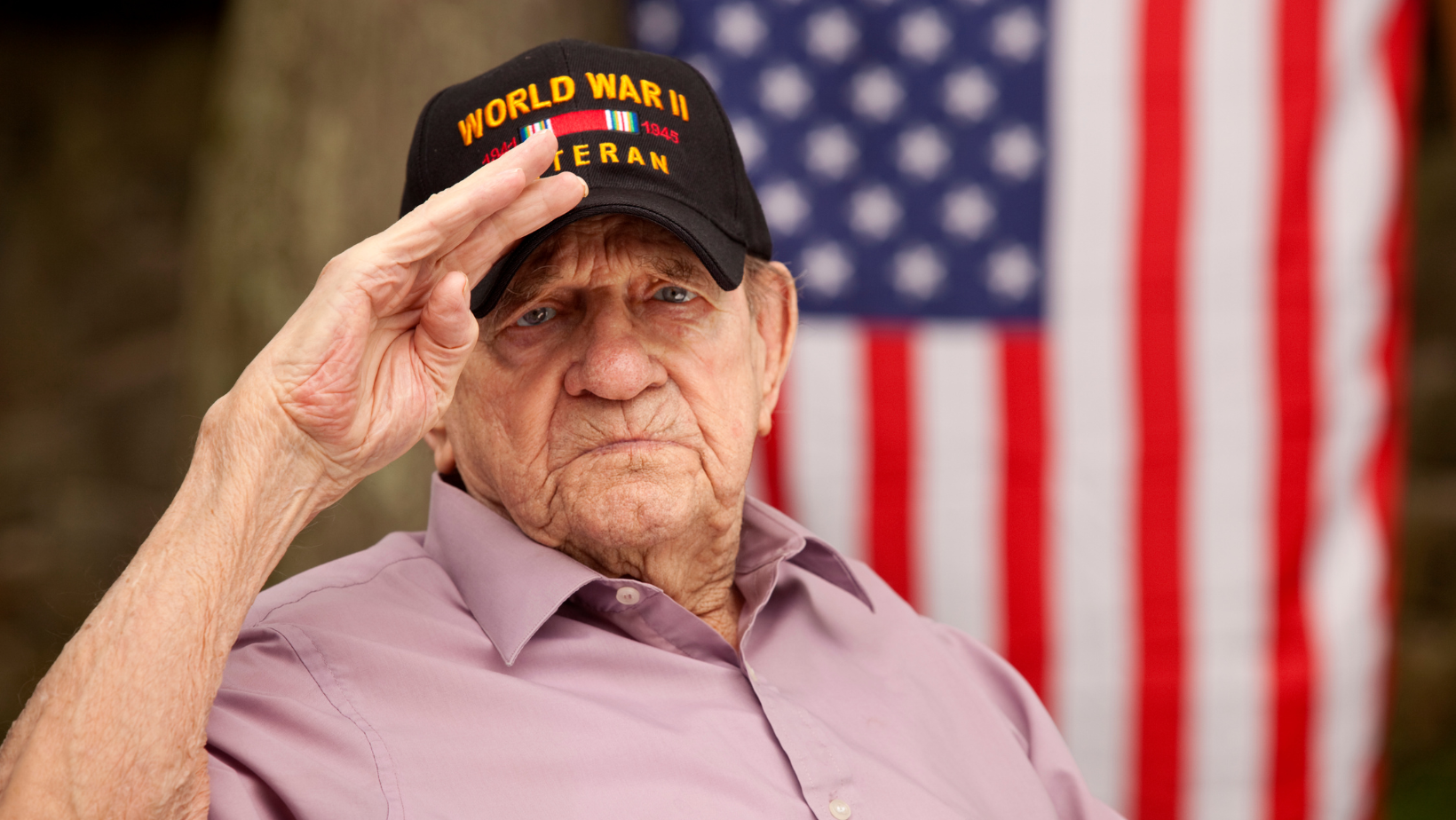 Senior veteran saluting with an American flag behind him