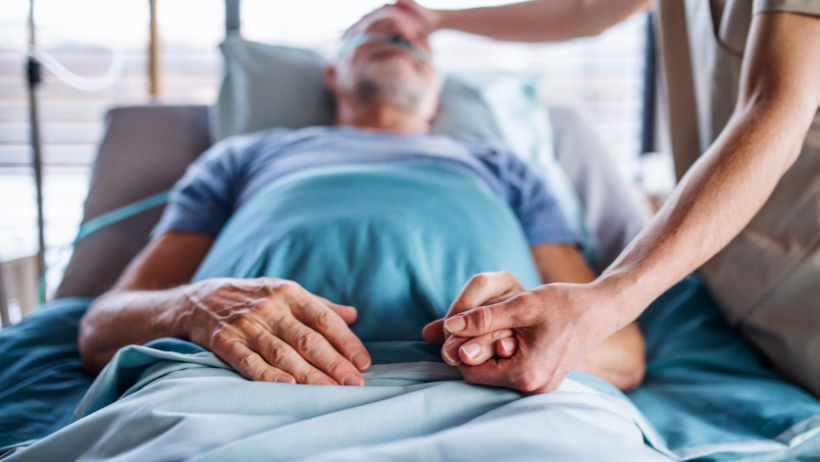 Senior man on hospice with a caregiver holding his hand