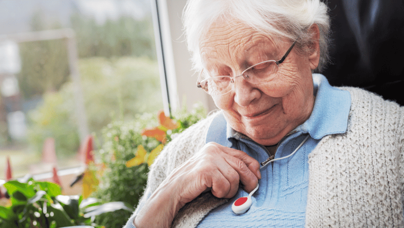 Senior woman sitting by a window and holding a medical alert device