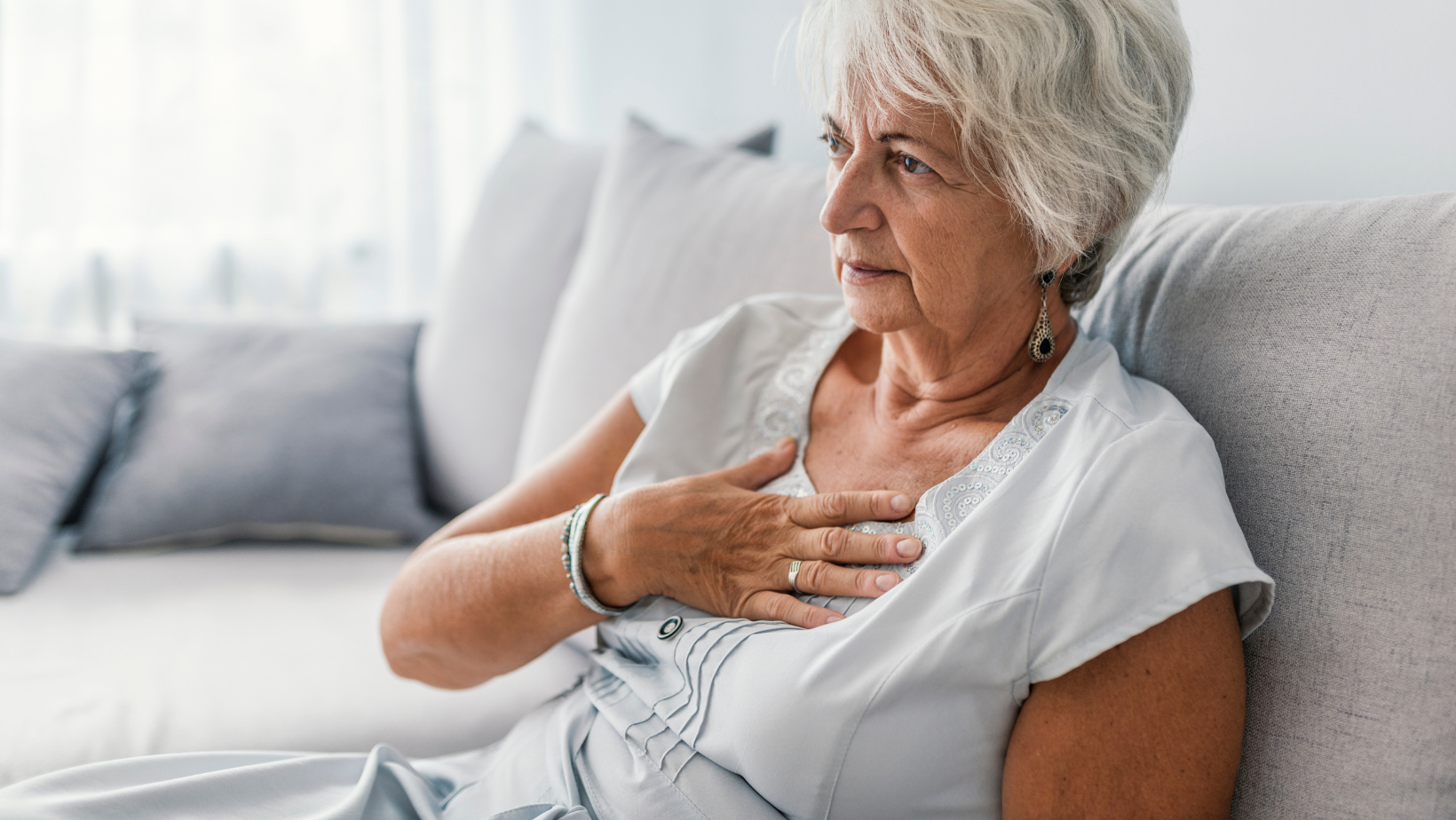 Senior woman holding her chest while sitting on a couch