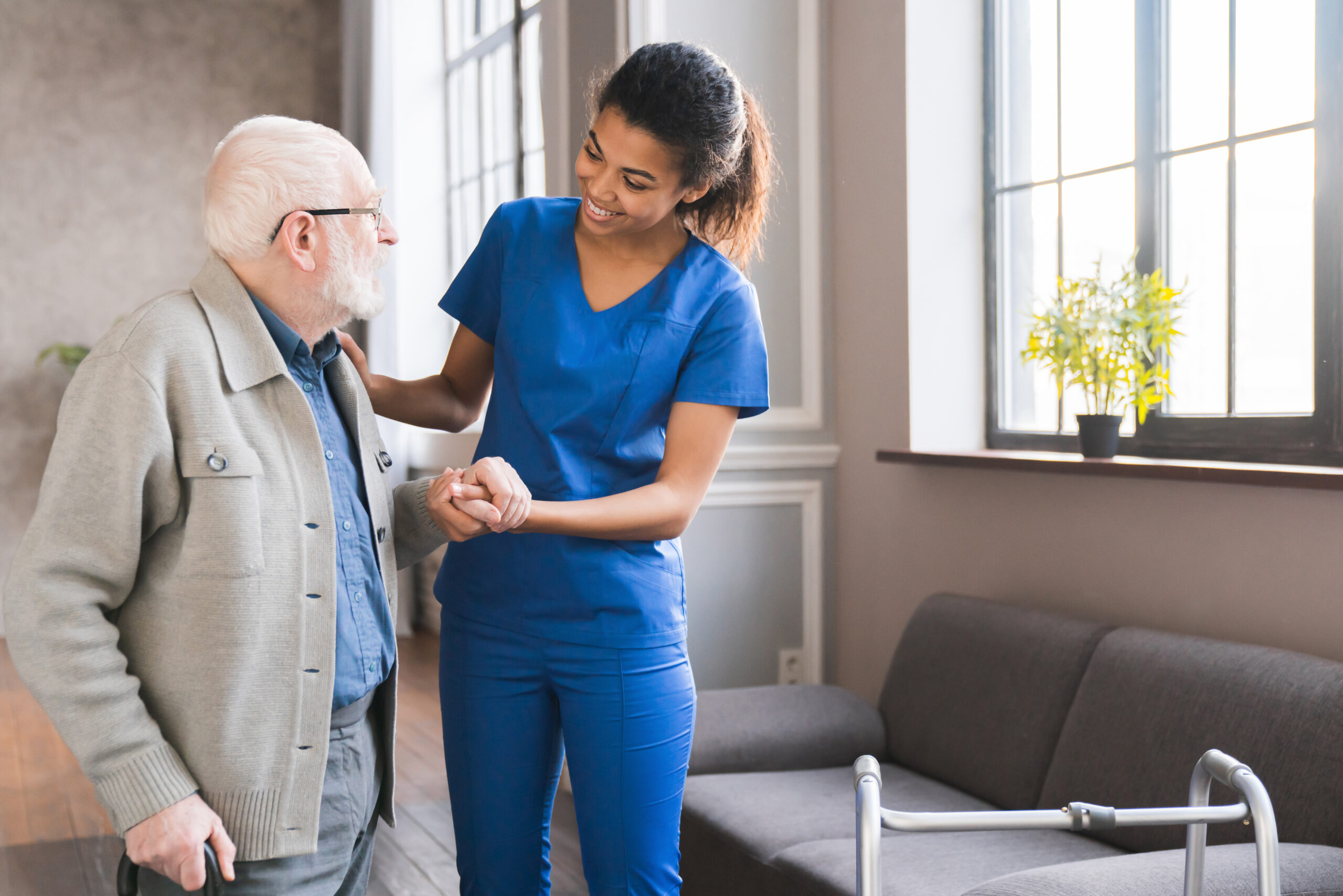 Young caring african nurse helping senior old elderly man grandfather walk
