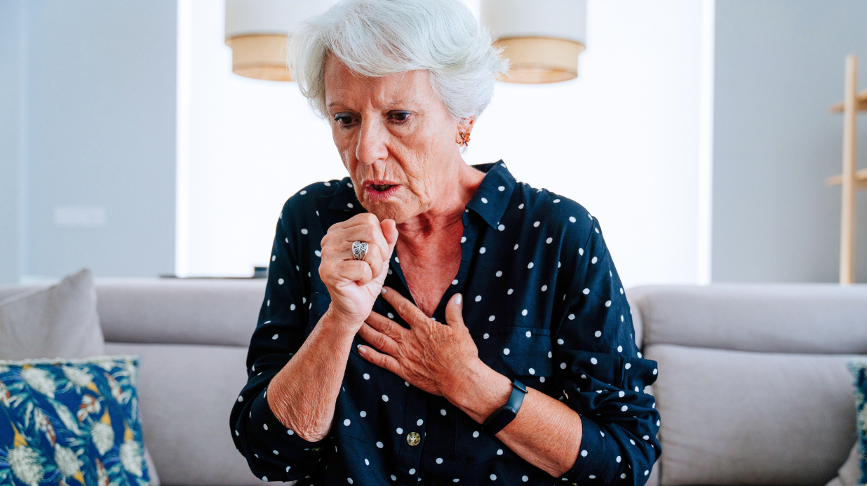 Senior woman coughing while sitting on couch