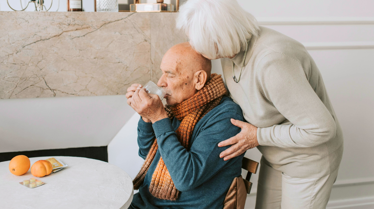 Senior woman helping her senior husband feel better with tea and oranges